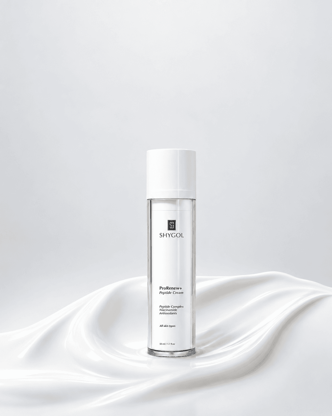 A Shygol ProRenew+ Peptide Cream bottle standing in a swirl of white cream against a soft grey backdrop, with no text or graphics added.