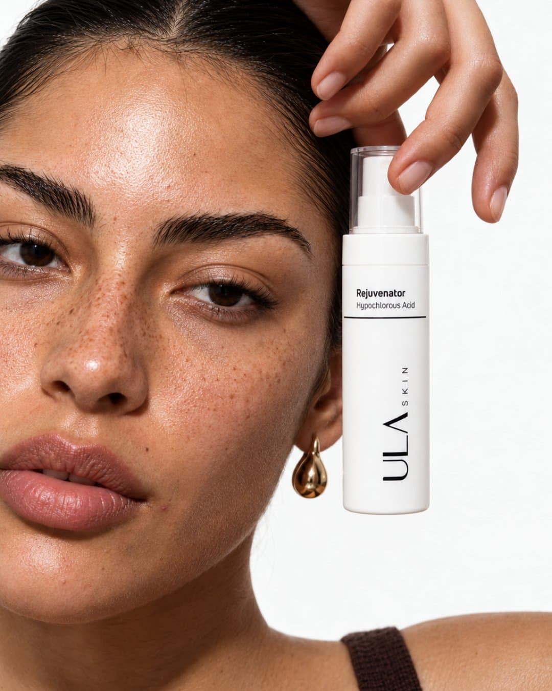 Close portrait of a freckled model raising a spray bottle beside her face