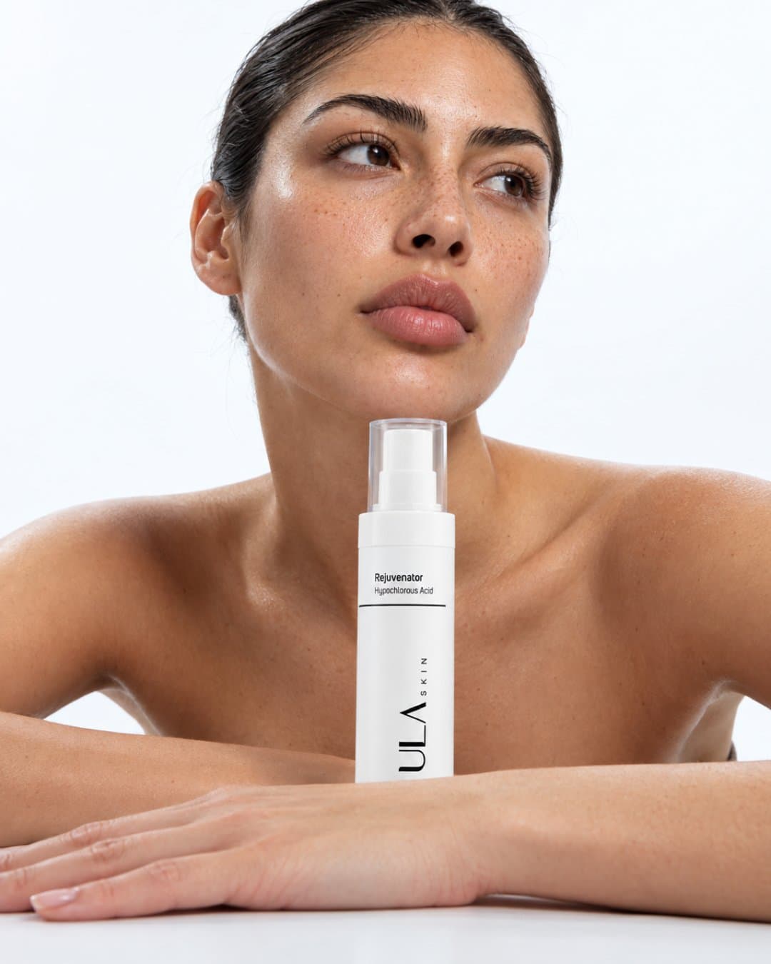 Model resting her chin on her arms beside a ULA spray bottle on a table