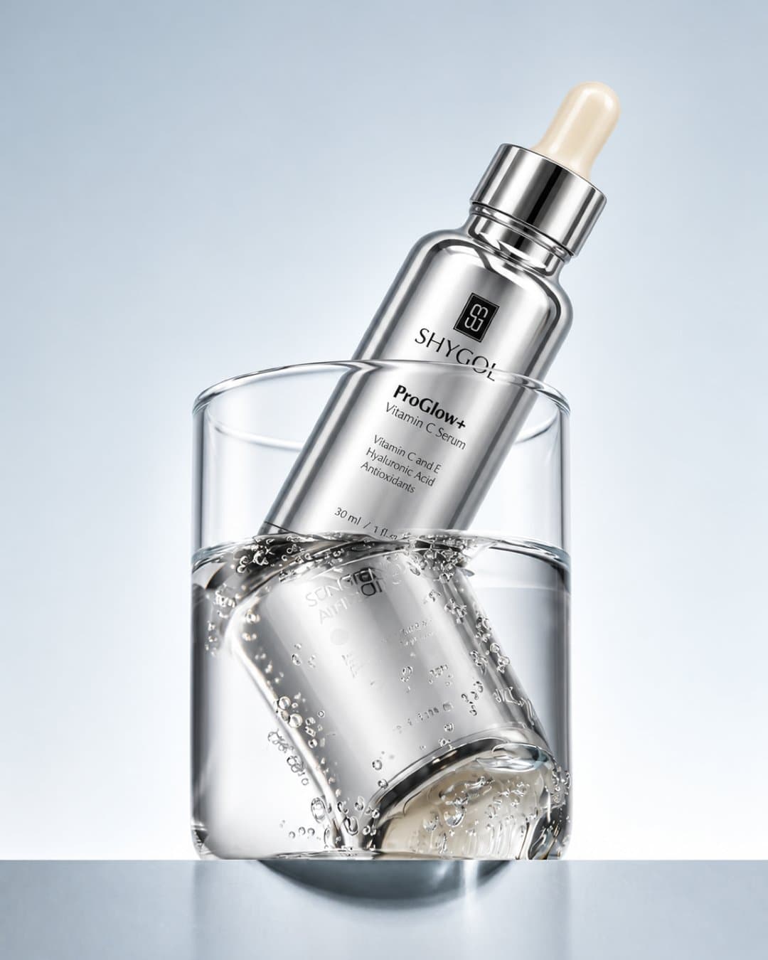 Silver Shygol ProGlow+ serum bottle tilted into a glass of water on a pale blue ground