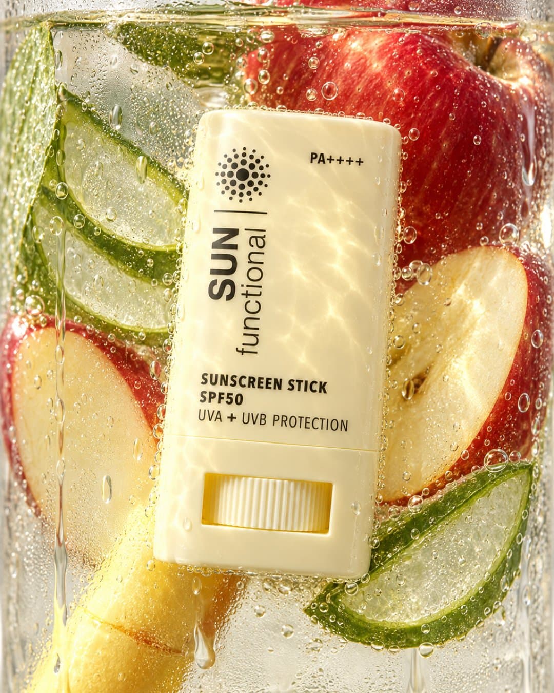 Sunscreen stick pressed against the glass in sparkling water with apple and aloe slices