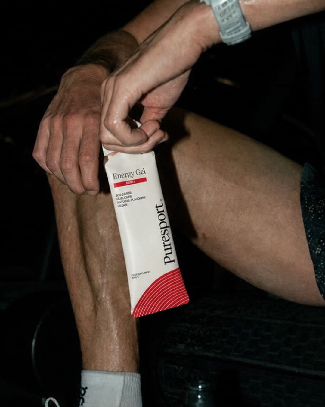 An athlete holding a Puresport Energy Gel sachet against his knee in a dark gym