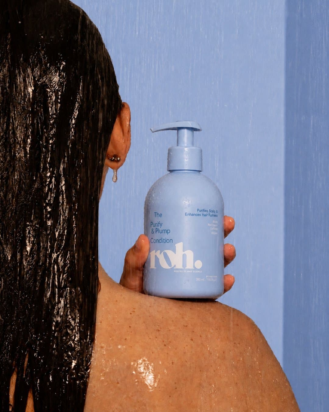Wet-haired model seen from behind holding a periwinkle ROH pump bottle against her shoulder