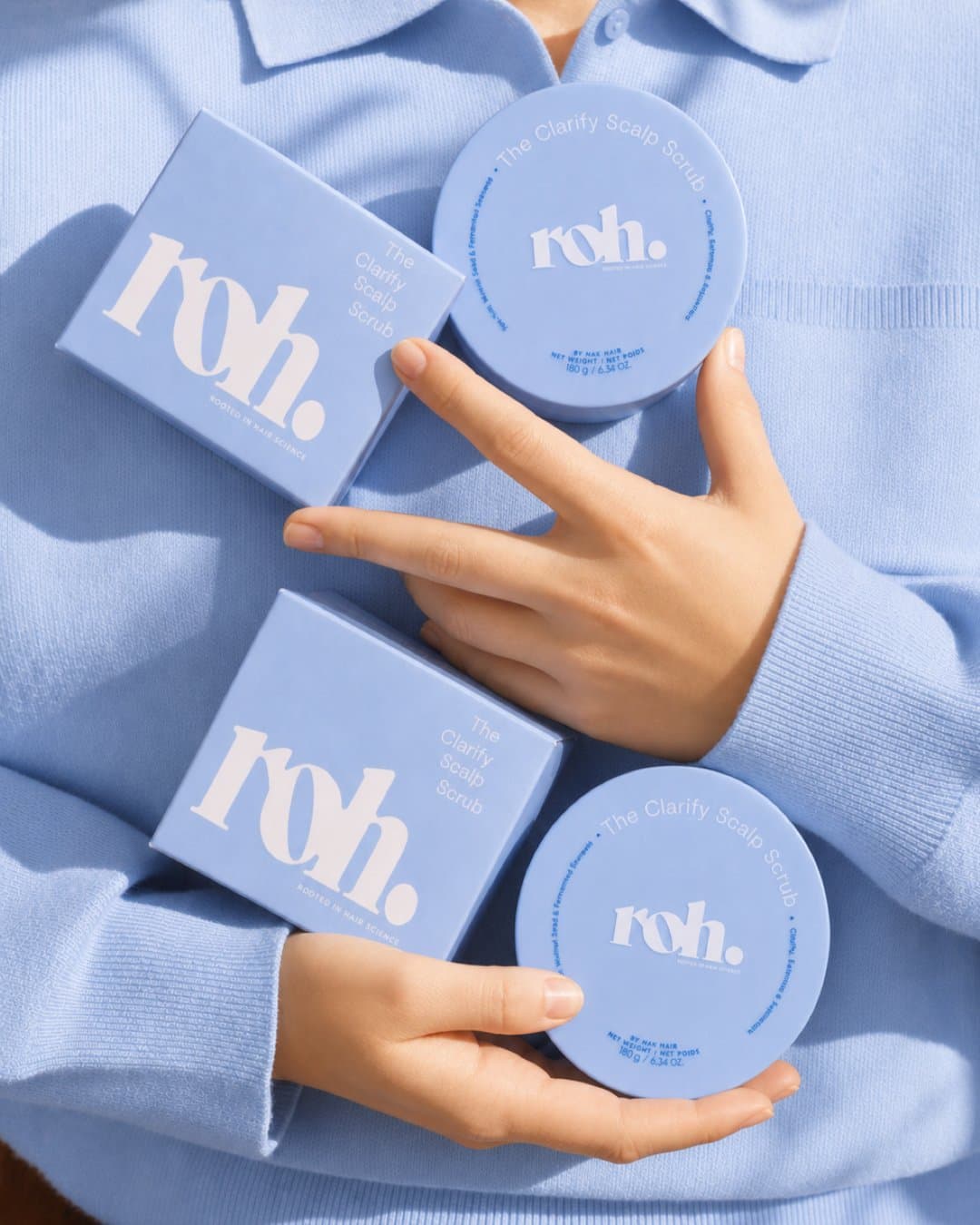 Hands holding ROH boxes and jars in periwinkle against a matching blue sleeve