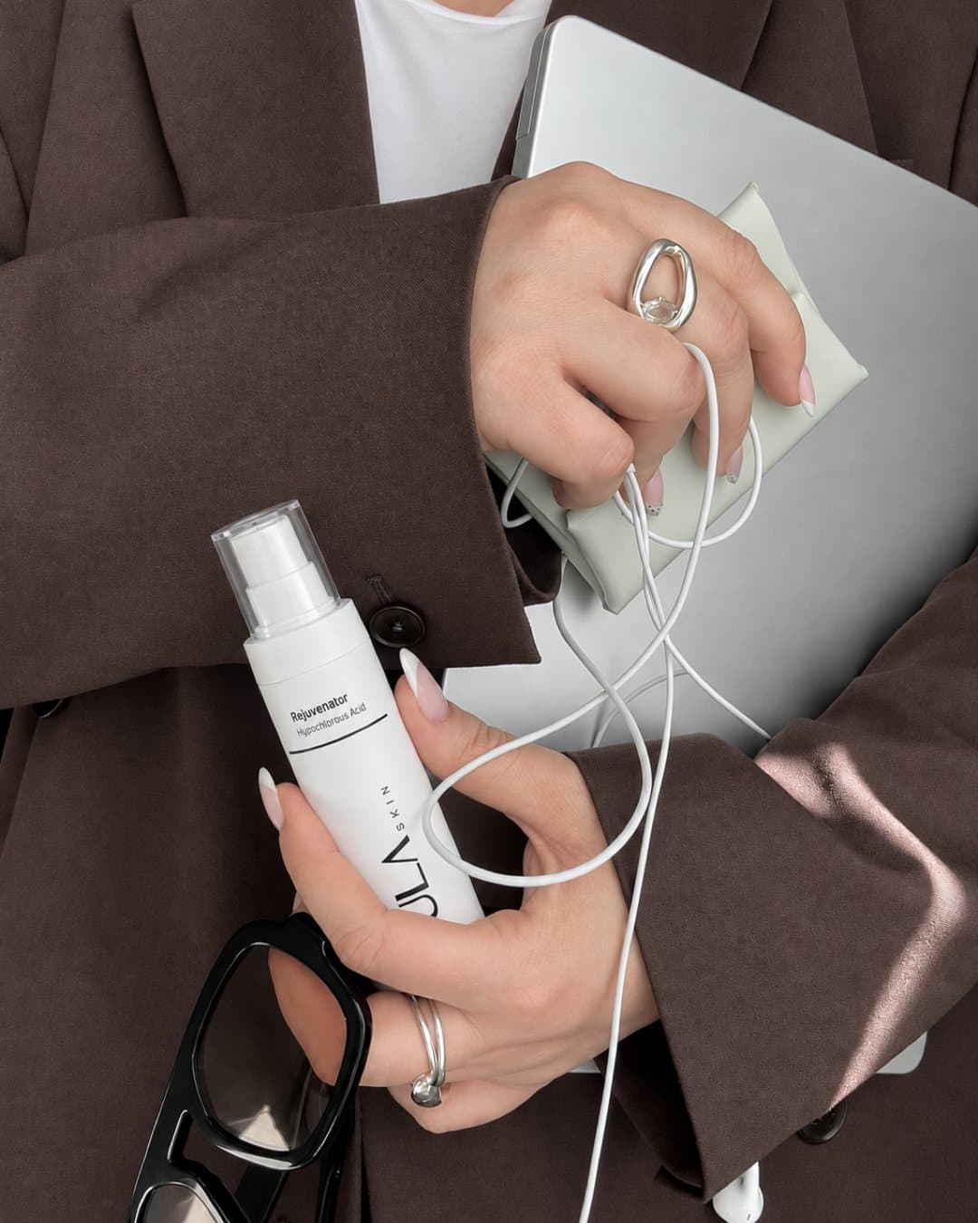 Hand holding a spray bottle against a blazer, with a laptop and earphones, in a workday scene