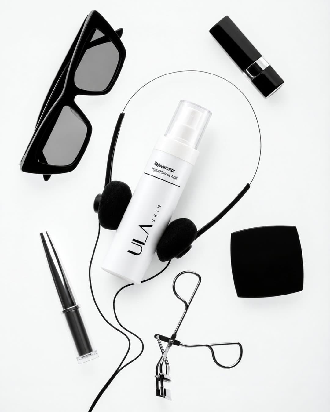 ULA Rejuvenator spray bottle on a white ground with sunglasses, headphones and makeup