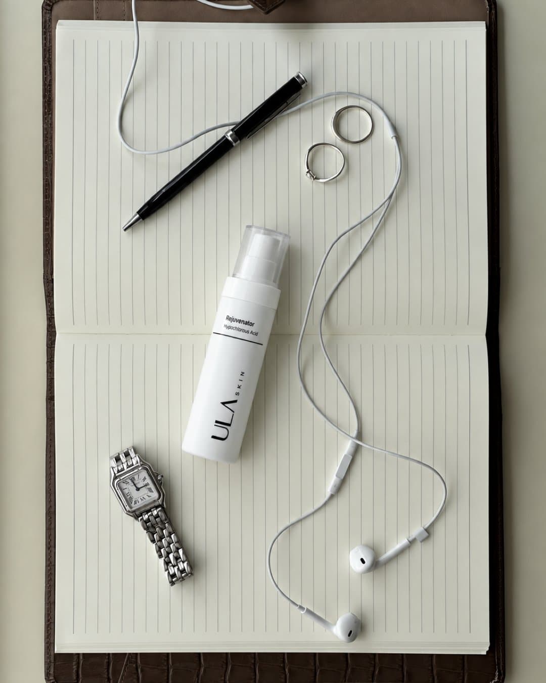 ULA Rejuvenator spray bottle on an open notebook with a pen, watch and earphones
