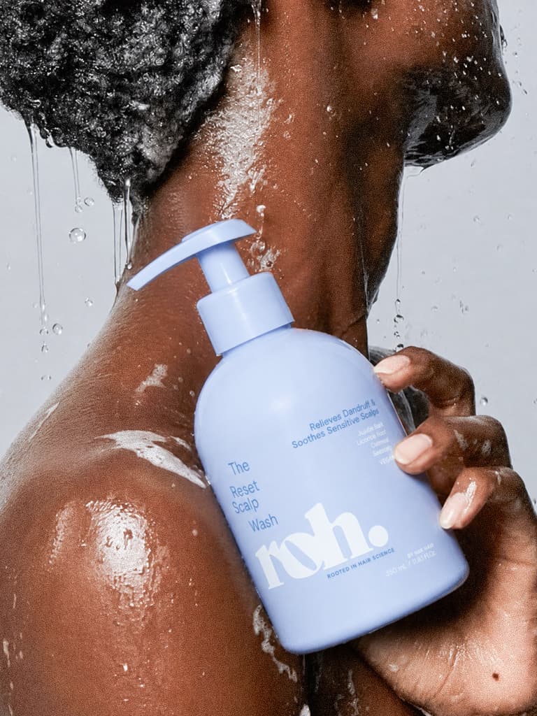 Close profile of a model rinsing scalp wash in the shower, periwinkle-blue pump bottle held to the shoulder