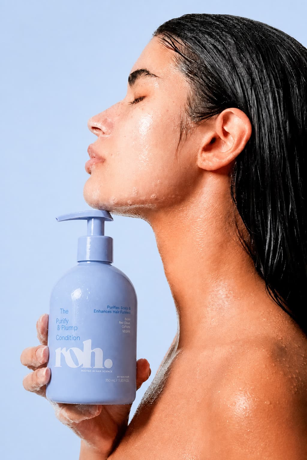 Model in profile holding a periwinkle condition bottle to her chin, wet hair and skin under studio light