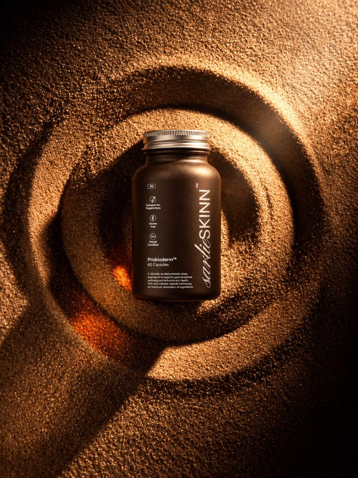 Probioderm bottle resting in a swirl of sand, low raking light