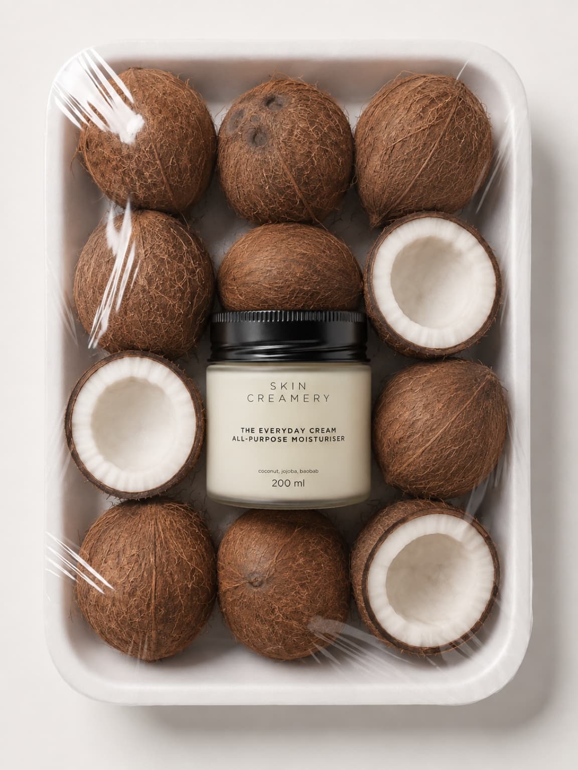 The Everyday Cream jar nestled in a supermarket produce tray among wrapped coconuts