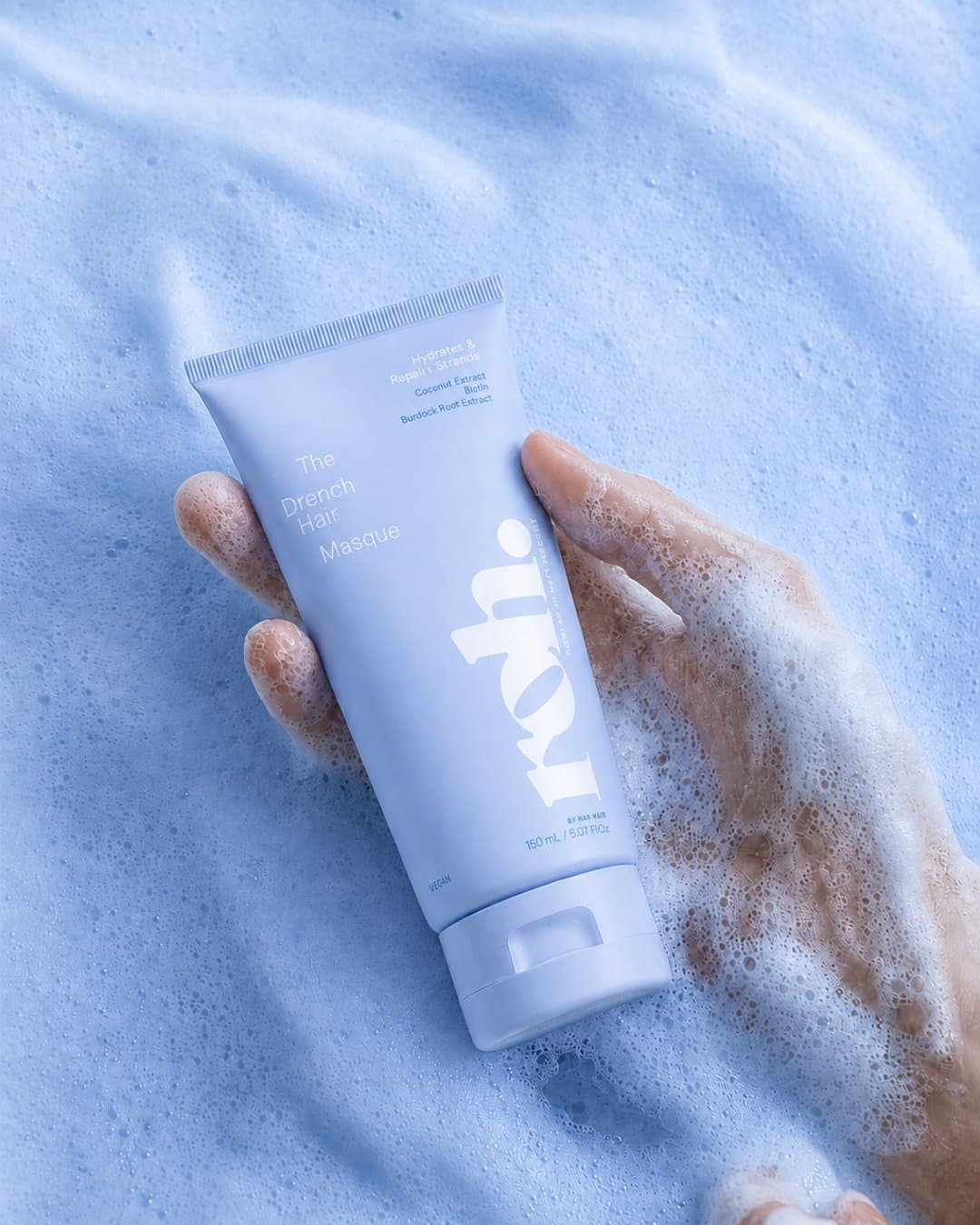 Hand holding a periwinkle ROH masque tube in white foam
