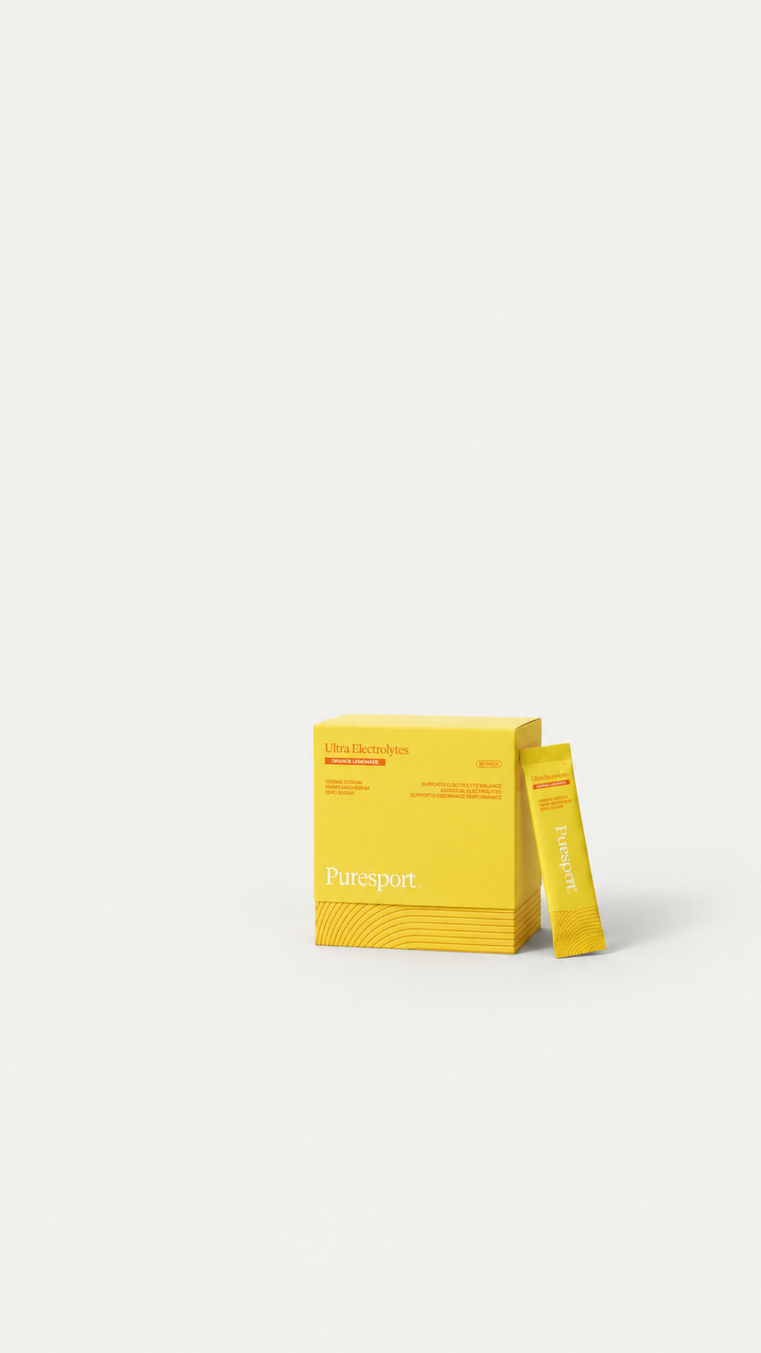 A pale studio ground with a yellow Puresport Ultra Electrolytes box and a sachet leaning against it at the lower right, and nothing else in the frame.